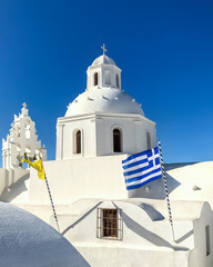 White temple building with a bell tower in island Santorini. National flag of Greece.