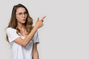 Doubting young woman wearing glasses pointing finger at copy space