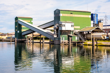 Fototapeta na wymiar Grain elevator with wagon and barge loading system of an agricultural cooperative on a canal in the river port of Strasbourg, France, with a train of hopper wagons waiting beneath.