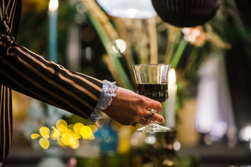 female hand with wine glass and decorated greenhouse in trendy christmas setting with dinner table, candles and christmas lights.