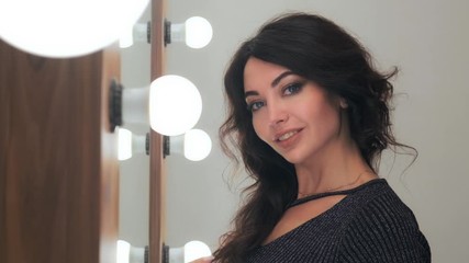 stylish young woman with beautiful professional hair styling posing in front of a mirror with light bulbs in a beauty salon.