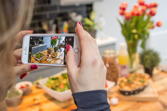 Woman with red nails shooting photos of food on a household table with her mobile phone for social media instagram healthy diet high protein food for a great body and lifestyle table flowers bread