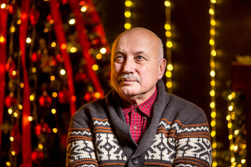 Obraz premium Portrait of grandfather is sitting near Cristmas tree at night at home