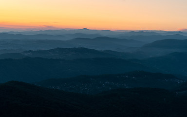 Panorama of a mountain landscape at sunset. Hills blue gradient background. Orange sky on the horizon. Misty evening in the mountains.