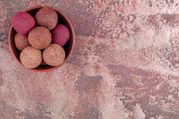 Homemade Colorful Raw Vegan Cocoa Energy Balls in Wooden Bowl on Marble Background. Healthy Chocolate Candy from Nuts and Dates. Concept of Natural Vegetarian Handmade Dessert. Top View. Copy Space