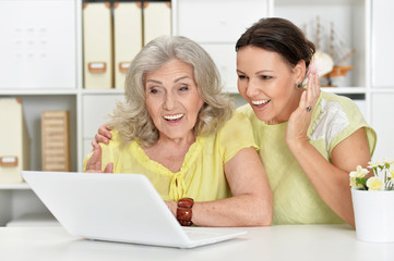 Portrait of mother and daughter sitting at table with laptop, at home