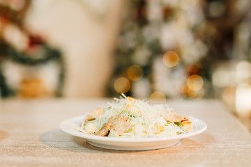 New Year 2020. Christmas table dinner time with salad decorated in New Year style on bokeh background. Christmas beautiful lights on gold warm background. Salad Caesar.