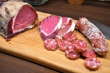 Slices of raw salted homemade ham or prosciutto and sausage on a wooden board with knife