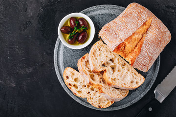 Italian ciabatta bread slices with olives on stone plate on dark concrete background