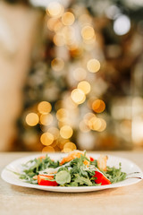 New Year 2020. Christmas table dinner time with salad decorated in New Year style on bokeh background. Christmas beautiful lights on gold warm background.