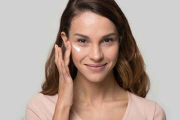 Head shot portrait beautiful young woman applying cosmetic cream