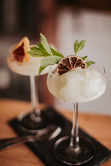 Two gin based sorbet cocktails on a black slate with tea spoon. Concept of refreshing cocktails and alcoholic drinks. Selective focus on the glasses. - obrazy, fototapety, plakaty