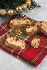 Traditional Italian Biscotti or Cantuccini cookies with hazelnuts, almonds, walnuts on a red-green napkin near the Christmas tree. Christmas and New Year baking.