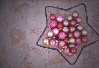 Star shaped glass vase with Christmas balls on a stone textured background. 