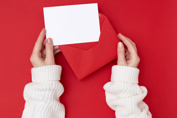 Women's hands holding an empty postcard and red envelope on the red background. Christmas concept