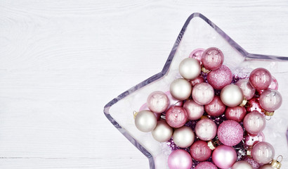 Star shaped glass vase with Christmas balls on a wooden white background. Close-up.