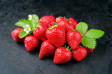 Fresh ripe strawberries offered as closeup on black rustic board as background with copy space