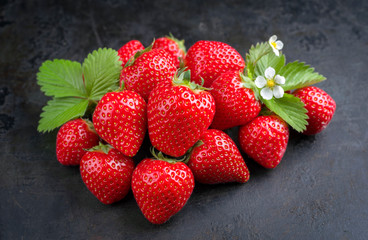 Fresh ripe strawberries offered as closeup on black rustic board as background