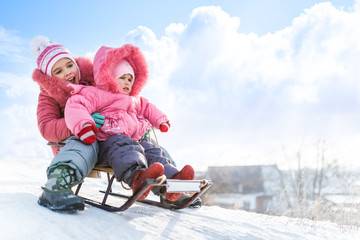 Happy small girls in pink winter clothing sledding downhill on snow