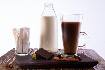A glass of coffee with chocolate on a tray, a bottle of milk and bags with sugar in the background on a white background.