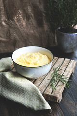   Creamy corn traditional polenta or mamaliga with butter. Served in white shallow dish on rustic wooden table with rosemary. Country style. Selective focus, copy space. Healthy organic food concept.