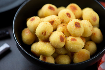 Close-up of italian pan fried stuffed potato gnocchi served in a black bowl, selective focus, studio shot