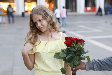 young girl refuses flowers from a street seller.  European girl with blue eyes and curly hair.