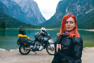 Close up portrait of female motobiker in protective turtle jacket. Touring motorcycle background. Extreme vacation, motorcyclist adventure lifestyle. Toblacher See, (Italian: Lago di Dobbiaco) Italy.