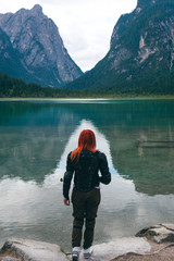 Red hair girl in body protection jacket turtle armor, walk adove the Alps mountain and lake. Vertical photo. Toblacher See, (Italian: Lago di Dobbiaco) a lake in South Tyrol, Italy.