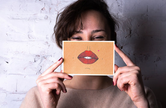 Woman (brown Eyes, Brown Hair) Is Holding A Postcard With Big Mouth And Nose