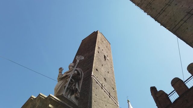 Perspective bottom view of Due Torri, symbol of city under blue sky in Bologna, Italy. Torre degli Asinelli and Torre Garisenda in historic downtown. Saint San Petronio statue, protector of the city.