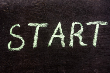 the inscription in chalk "start" on a wooden, black background. Close-up.