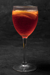 Aperol spritz cocktail glass on stone table with oranges. Dark mode. 