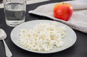 cottage cheese in a plate, an apple and a glass of water on a wooden table. Healthy eating concept.