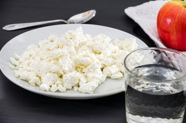 cottage cheese in a plate, an apple and a glass of water on a wooden table. Healthy eating concept.