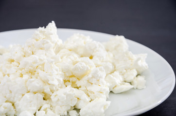 white cottage cheese in a white plate on a black table. View from above. Close-up.