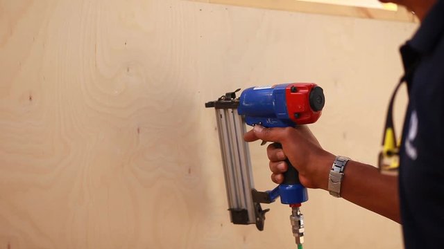 wooden carpenter using air compressor nail gun.The worker makes finishing works of walls with white wooden board