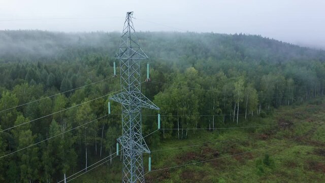 Flying around electricity pylon in green forest in foggy morning. High-voltage power lines in Siberia, Russia