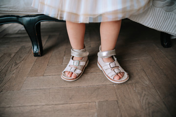 The legs of unrecognizable little girl in pink sandals wearing the wrong standing on a wooden floor.