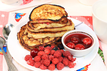 Delicious russian pancakes with cherries and strawberries and a mug of milk on a bright table, top view, selective focus. Traditional Russian pancakes, natural food, jam and berries with milk.