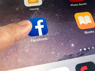 Macro image of a finger about to click the Facebook icon on an iPad screen