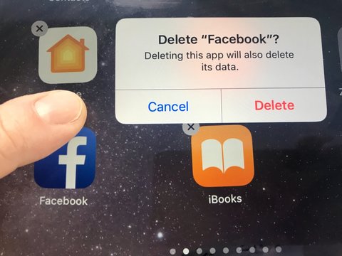 Macro image of a finger about to delete the Facebook app from an iPad screen - might be due to data privacy issues, Facebook is currently facing