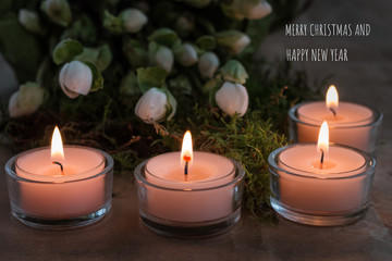 Fototapeta na wymiar Christmas card with four burning tealights, Christmas rose buds, moss and Christmas and New Year´s greetings in white letters g 
