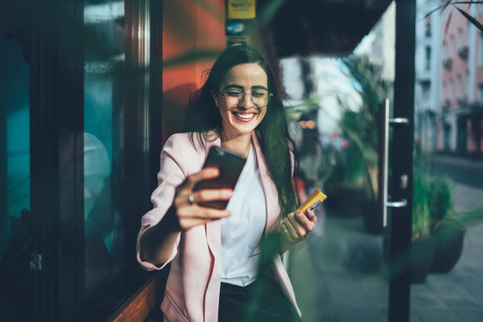 Happy Spanish woman in casual wear clicking selfie pictures via front camera on cellphone gadget, positive cheerful hipster girl smiling at camera for taking photos of herself enjoying free time