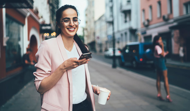Half length portrait of cheerful Spanish woman in casual outfit enjoying free time for caffee to go, positive millennial woman in spectacles for eyes protection smaling at camera during cell phoning - Powered by Adobe