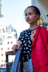 Beautiful teenager girl on a background of a city street in a bright red jacket.