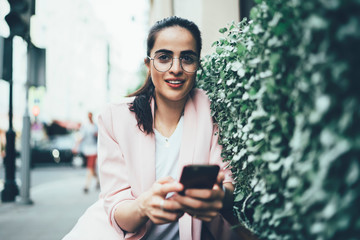Attractive hipster girl in spectacles for provide eyes protection looking away and thinking on name title for publication in social web page connecting to public internet during travel trip