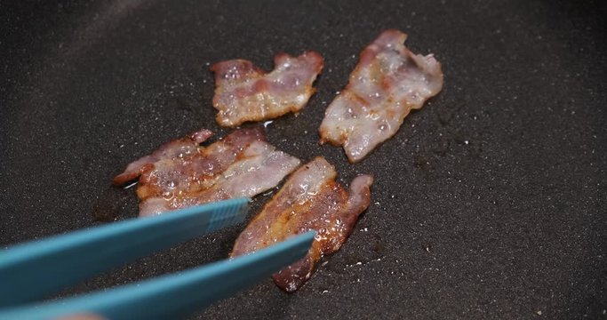 Fried slices of bacon are removed from hot pan, man is preparing unprofitable breakfast, slices of pork, four slices, hissing oil, butter, cholesterol, calories, poor nutrition, wife on business trip