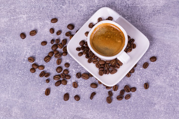 Hot coffee in a cup, coffee beans are scattered nearby. View from above