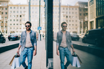 Handsome caucasian male buyer carrying bags with purchases satisfied with his job, happy hipster...